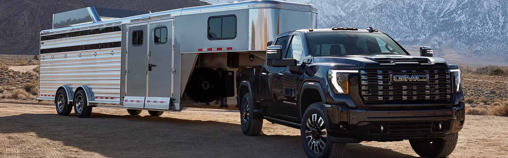 2025 GMC Sierra HD pickup truck towing a trailer in a rugged mountain landscape, showcasing powerful towing capability and durability.