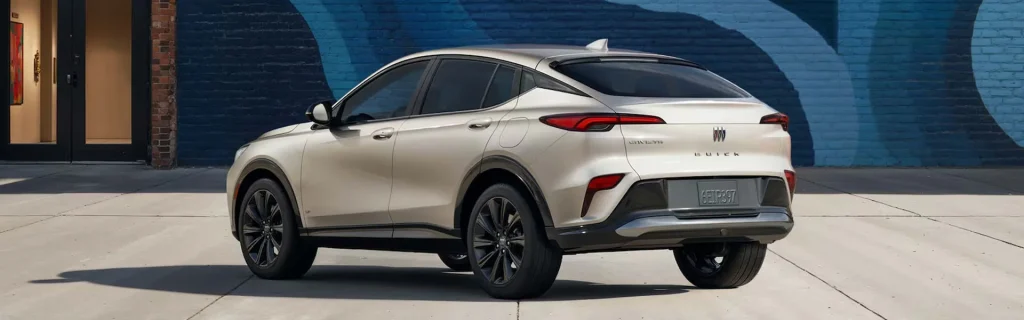The image shows a Buick Envista crossover SUV parked on a city street. The vehicle is positioned against a colorful brick wall, highlighting its sleek, modern design.