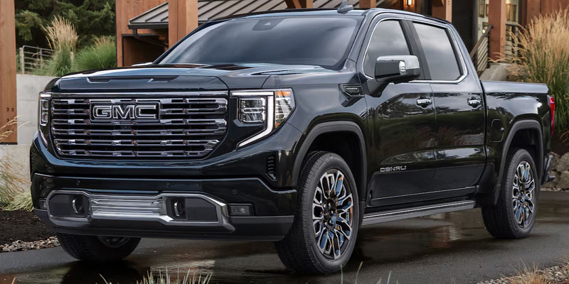 2026 GMC Sierra 1500 Denali pickup truck parked outside a modern home in Corpus Christi, TX, showcasing its bold grille, premium design, and upscale styling.