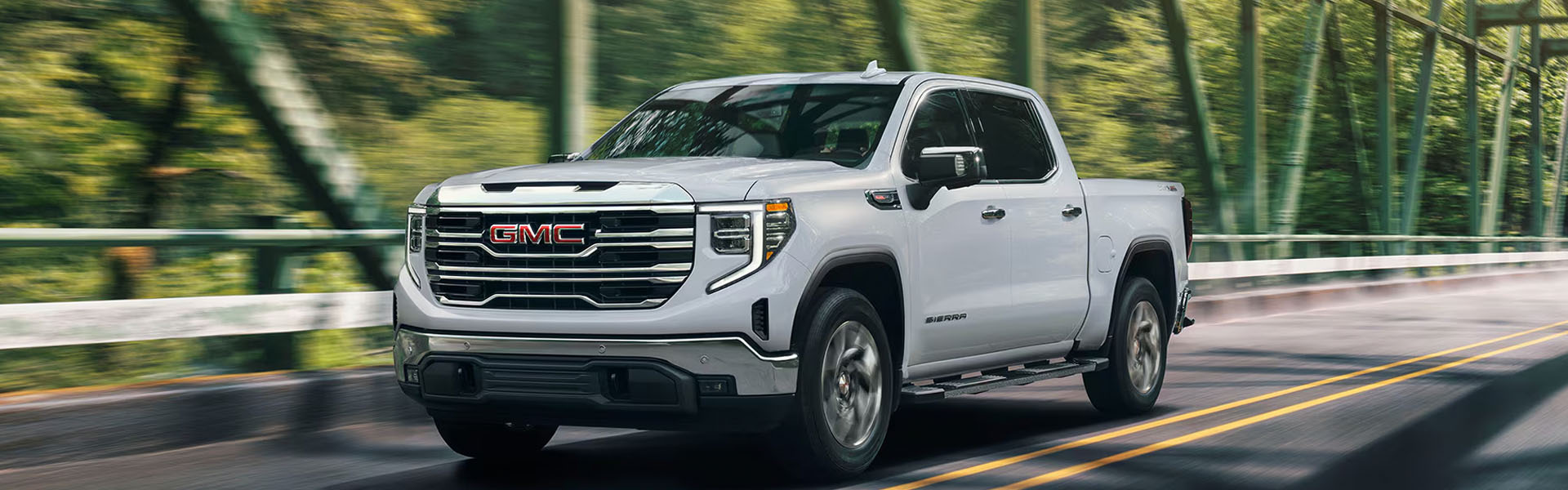 2026 GMC Sierra 1500 Elevation driving on a bridge surrounded by trees.